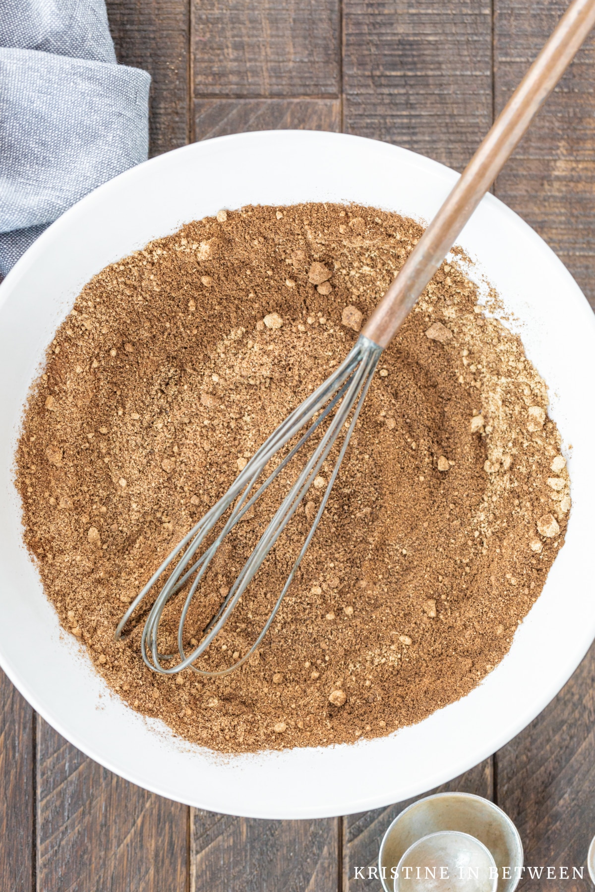 Spices whisked together on a white plate with an old whisk laying on top.