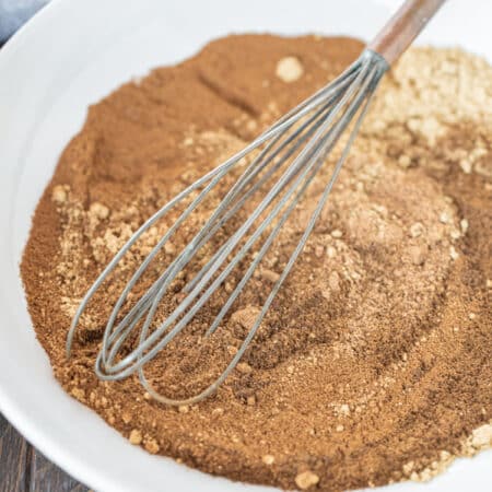 Spices whisked together on a white plate with an old whisk.