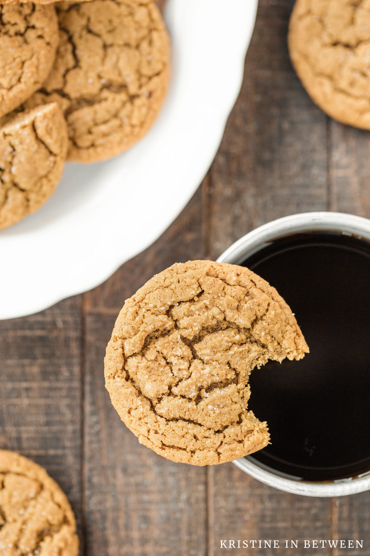 A cookie with a bite out of it balancing on the rim of a coffee cup.