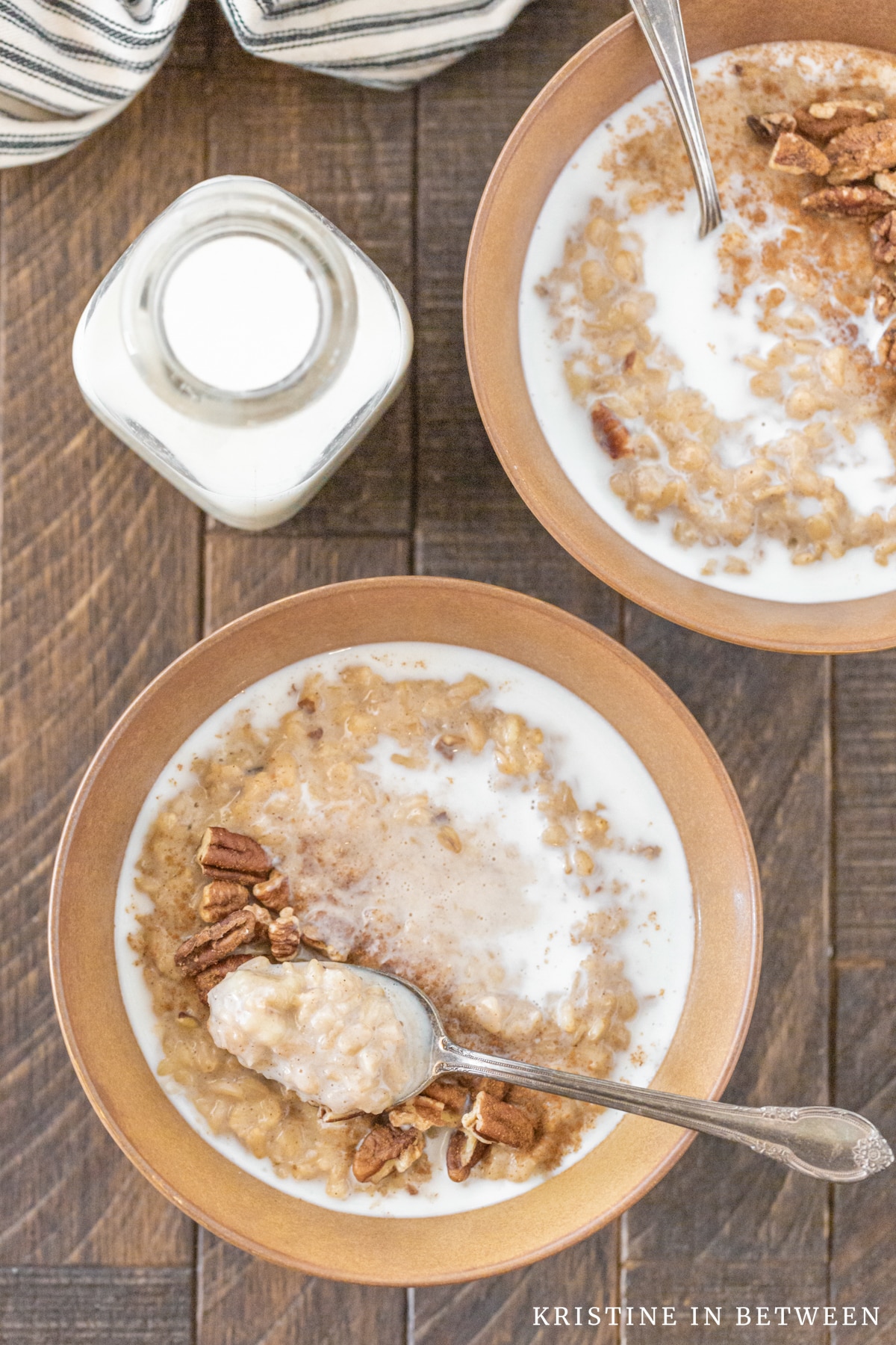 Two bowls of banana pecan oatmeal with spoons in them, drizzled with milk.