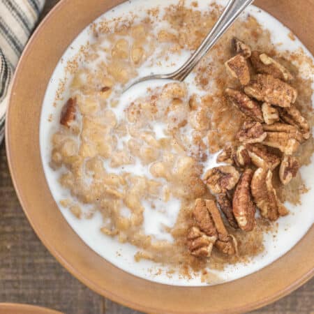 A bowl of banana pecan oatmeal with a spoon it, topped with chopped pecans and milk.