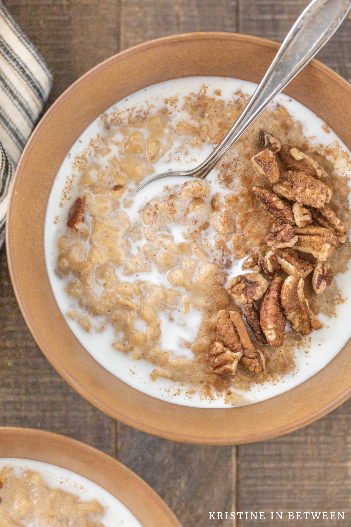 A bowl of banana pecan oatmeal with a spoon it, topped with chopped pecans and milk.
