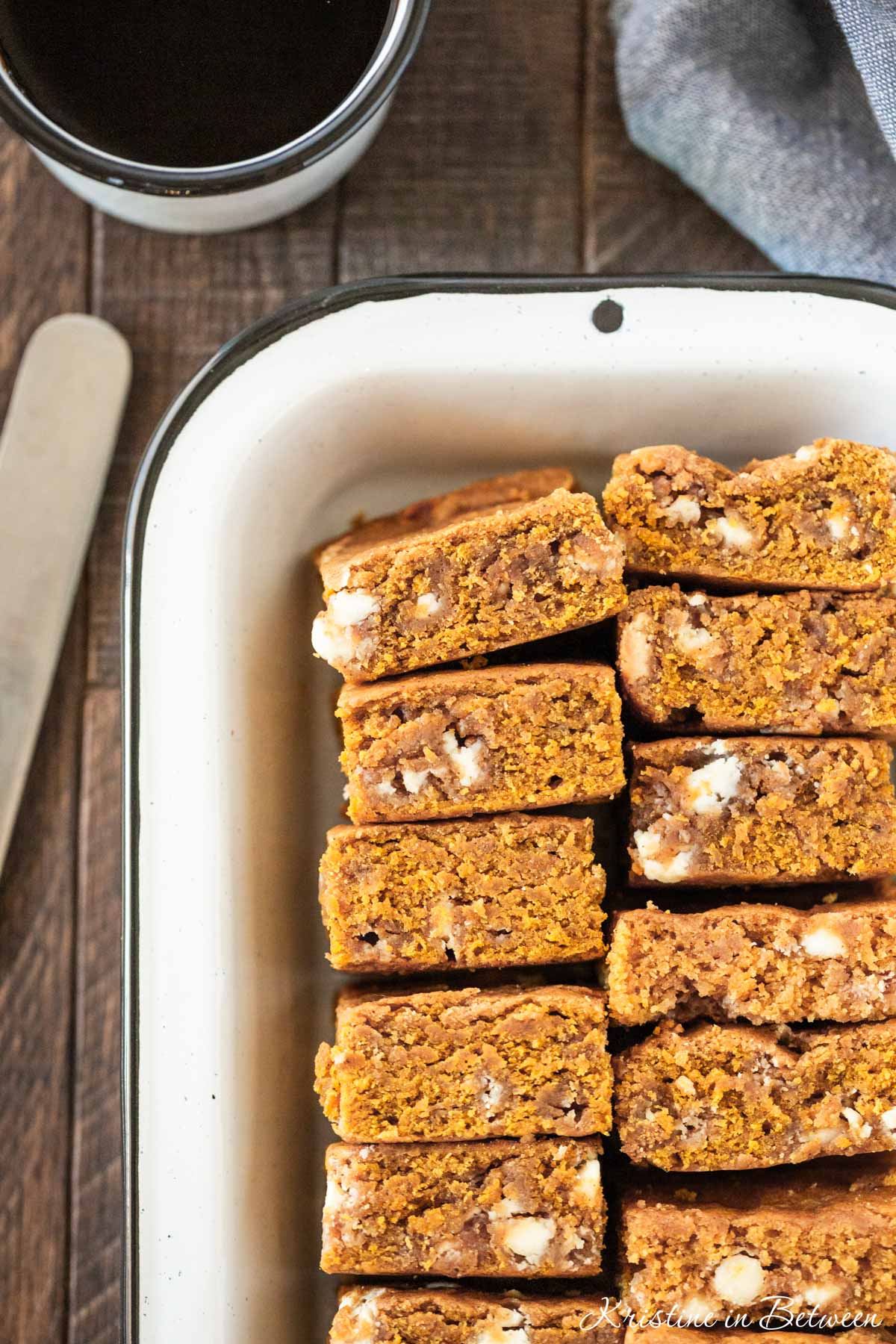 A pan of pumpkin blondies with white chocolate chips in them and a knife sitting next to them.