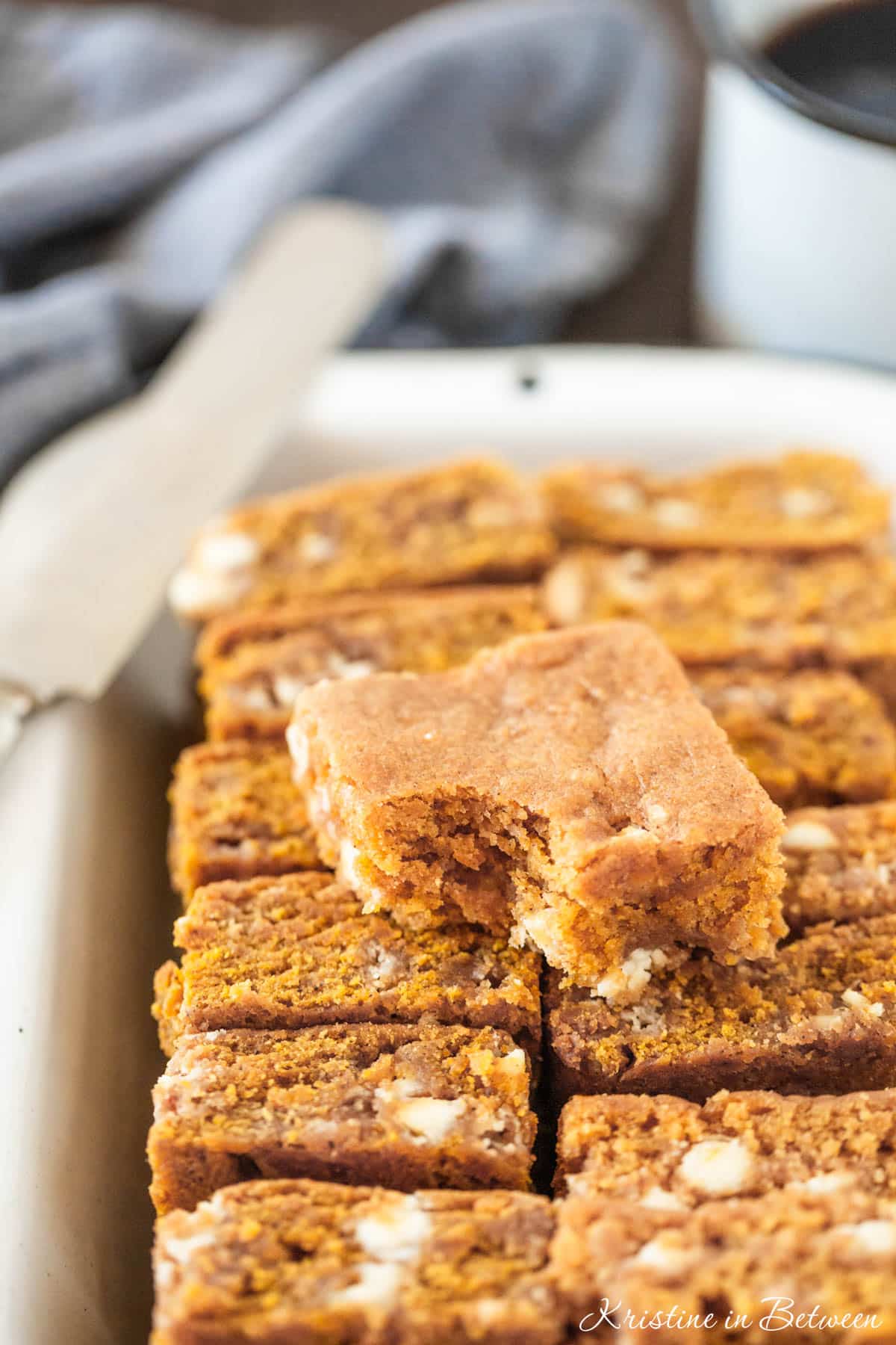 A pan of pumpkin blondies with white chocolate chips in them and a knife sitting next to them.