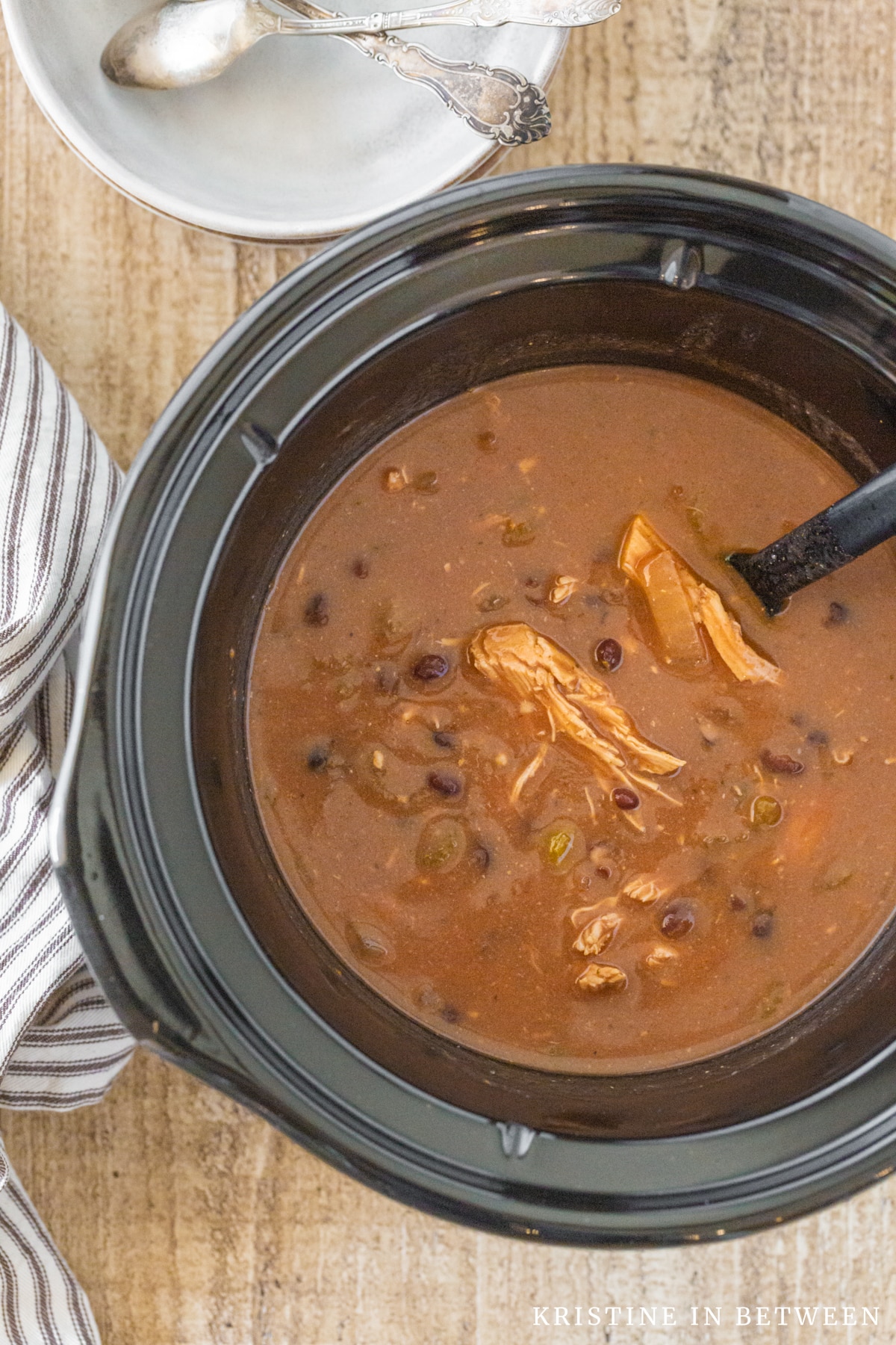 Chicken enchilada soup sitting in the crock of a Crock-pot with bowls and spoons in the background.