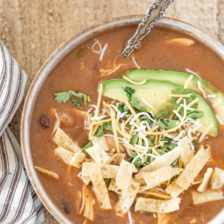 A bowl of chicken enchilada soup topped with cheese, tortilla strips, and avocado.