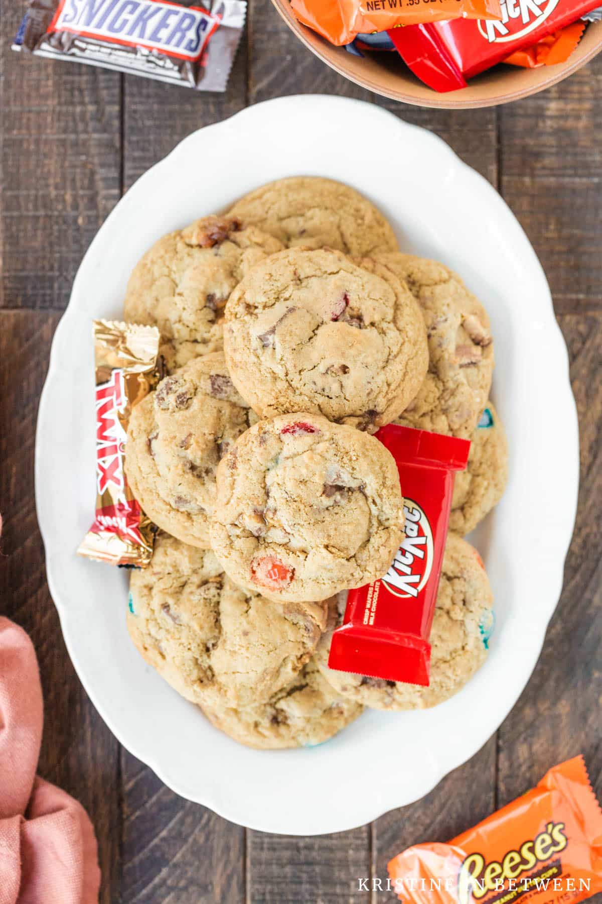 Cookies stacked up on a platter with candy in the background.