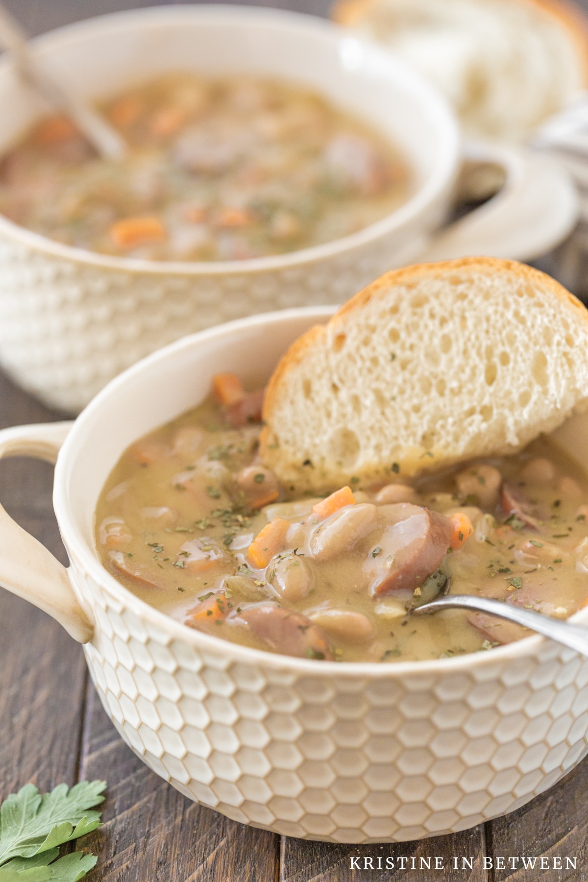 A bowl of soup with a spoon in it sitting with a piece of bread.