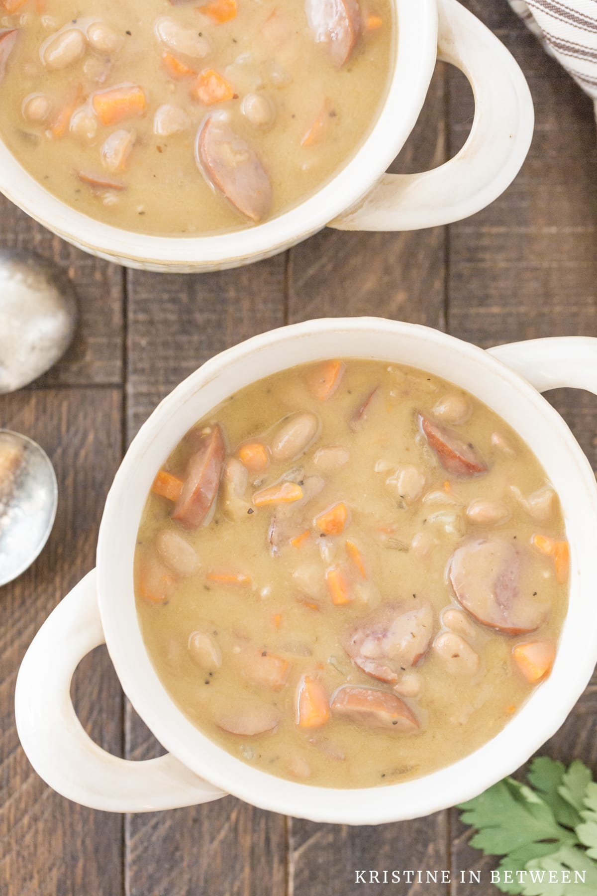 Two bowls of kielbasa and white bean soup sitting with two spoons.