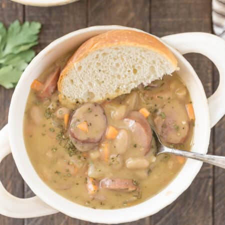 A bowl of kielbasa soup sitting a piece of bread and a spoon.