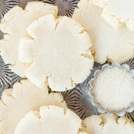Paradise Bakery sugar cookies stacked upon an old cookie sheet with a small bowl of sugar.