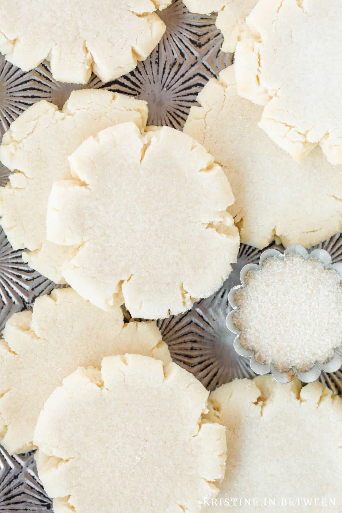 Cookies laying on a cookie sheet with a small bowl of sugar nestled in with them.