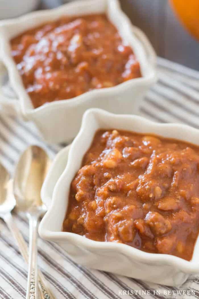 A bowl of pumpkin chili sitting with a spoon and a brown striped napkin.