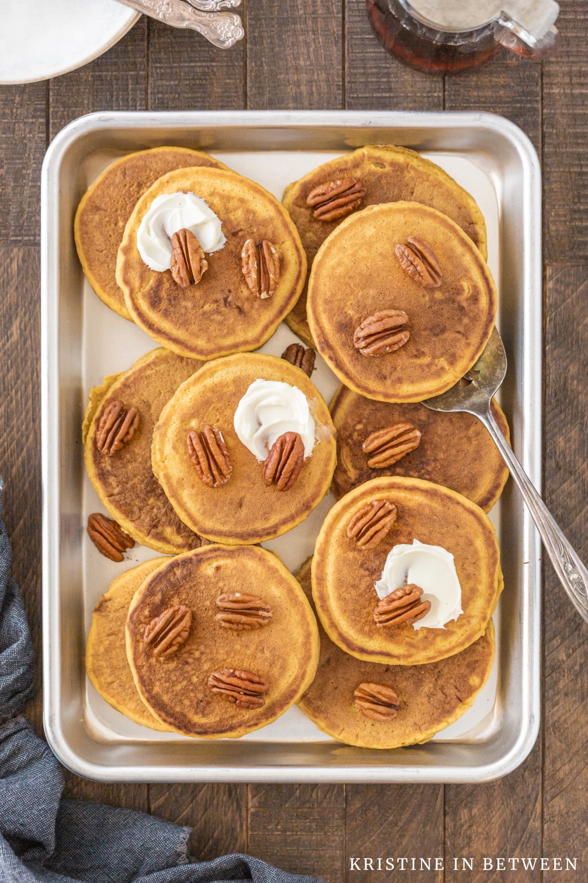 Pancakes laying on a baking sheet with pecans and butter on top.