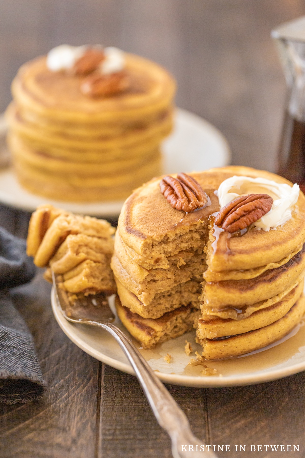 Pancakes stacked upon a plate with syrup drizzled on top and a bite cut out of them.