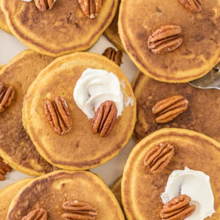 Pancakes stacked up on a try with pecans and butter on top.