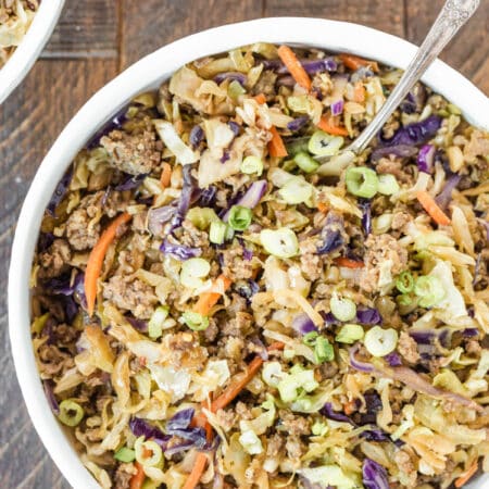 Sausage and cabbage in a white bowl with a fork in it and a small dish of soy sauce in the background.