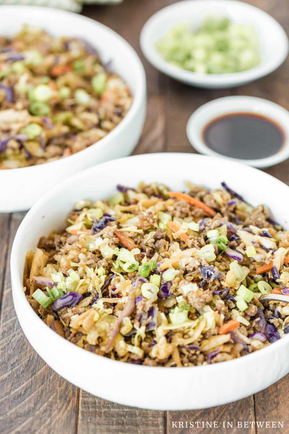 A bowl of sausage and cabbage with a bowl of soy sauce in the background.