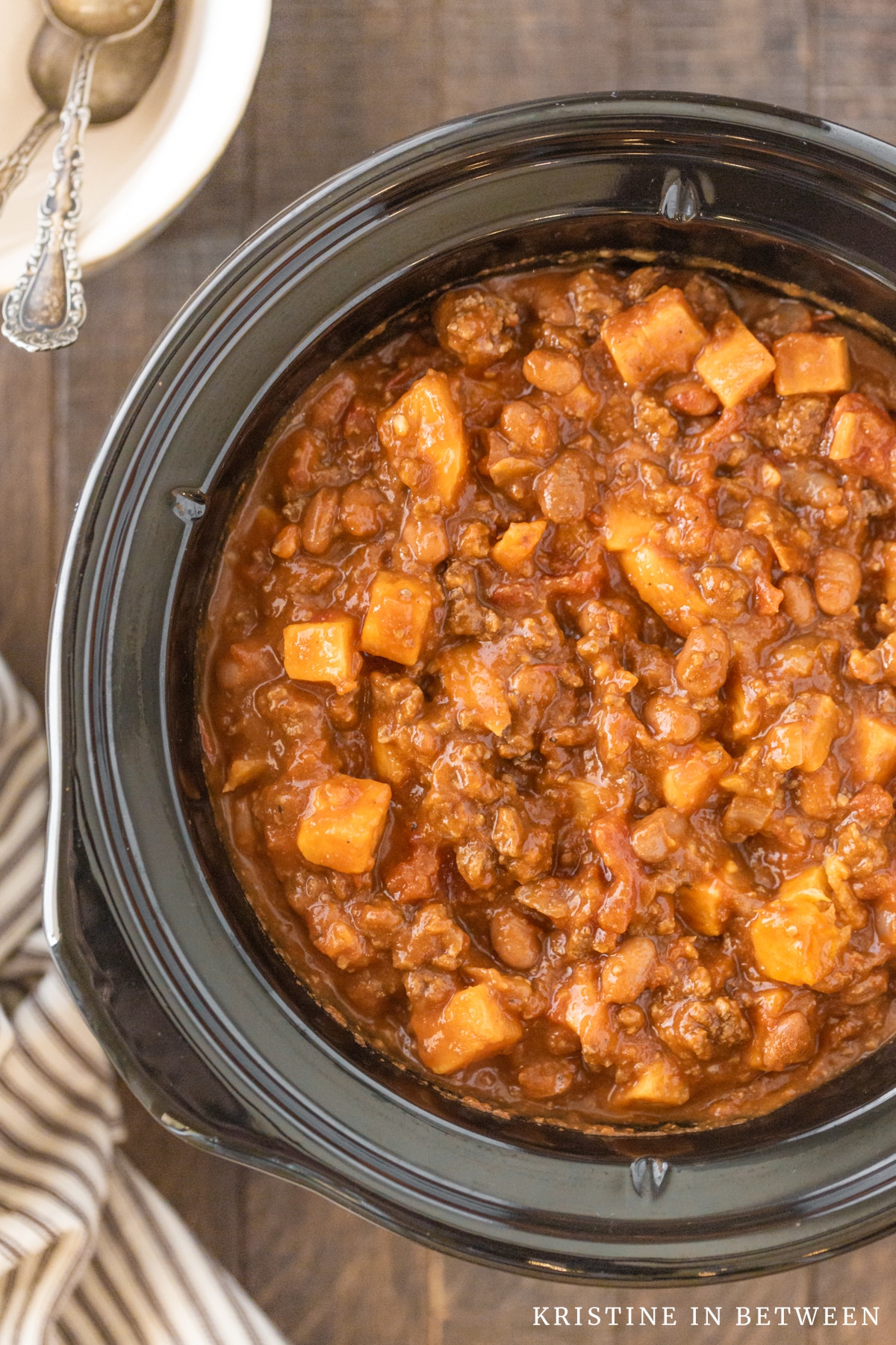 Cooked chili in the crock of a Crock-pot with two bowls and spoons in the background.