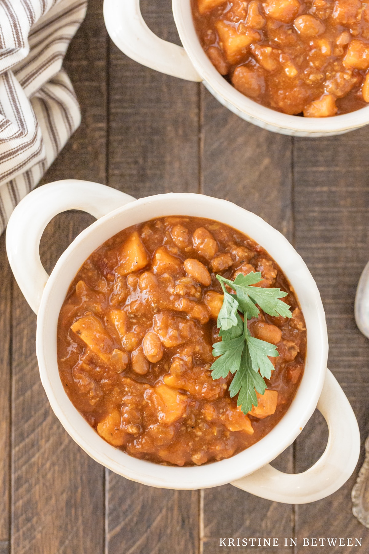 A bowl of chili with parsley on top and a spoon sitting next to it.