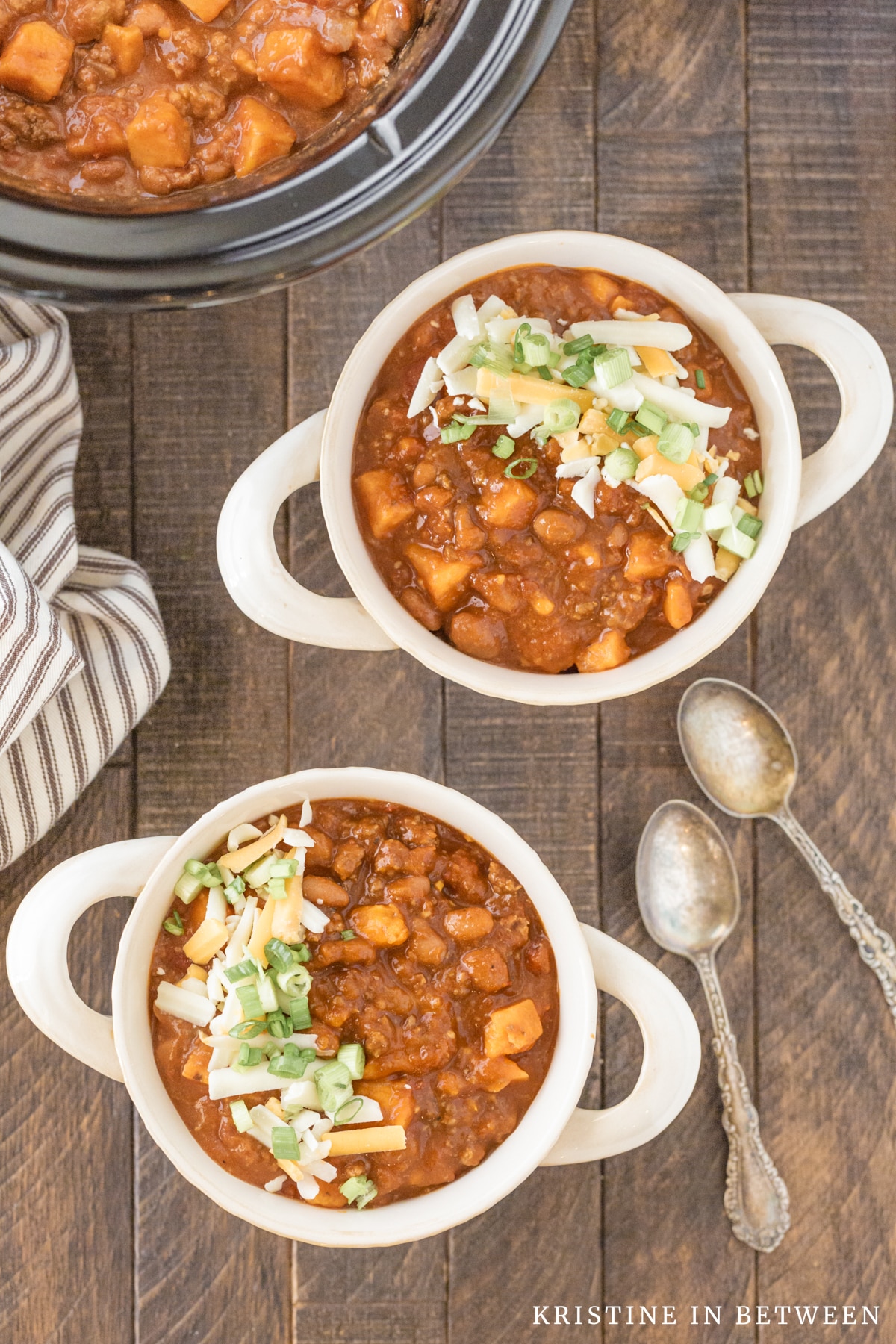 Two bowls of chili with two spoons and a Crock-pot in the background.