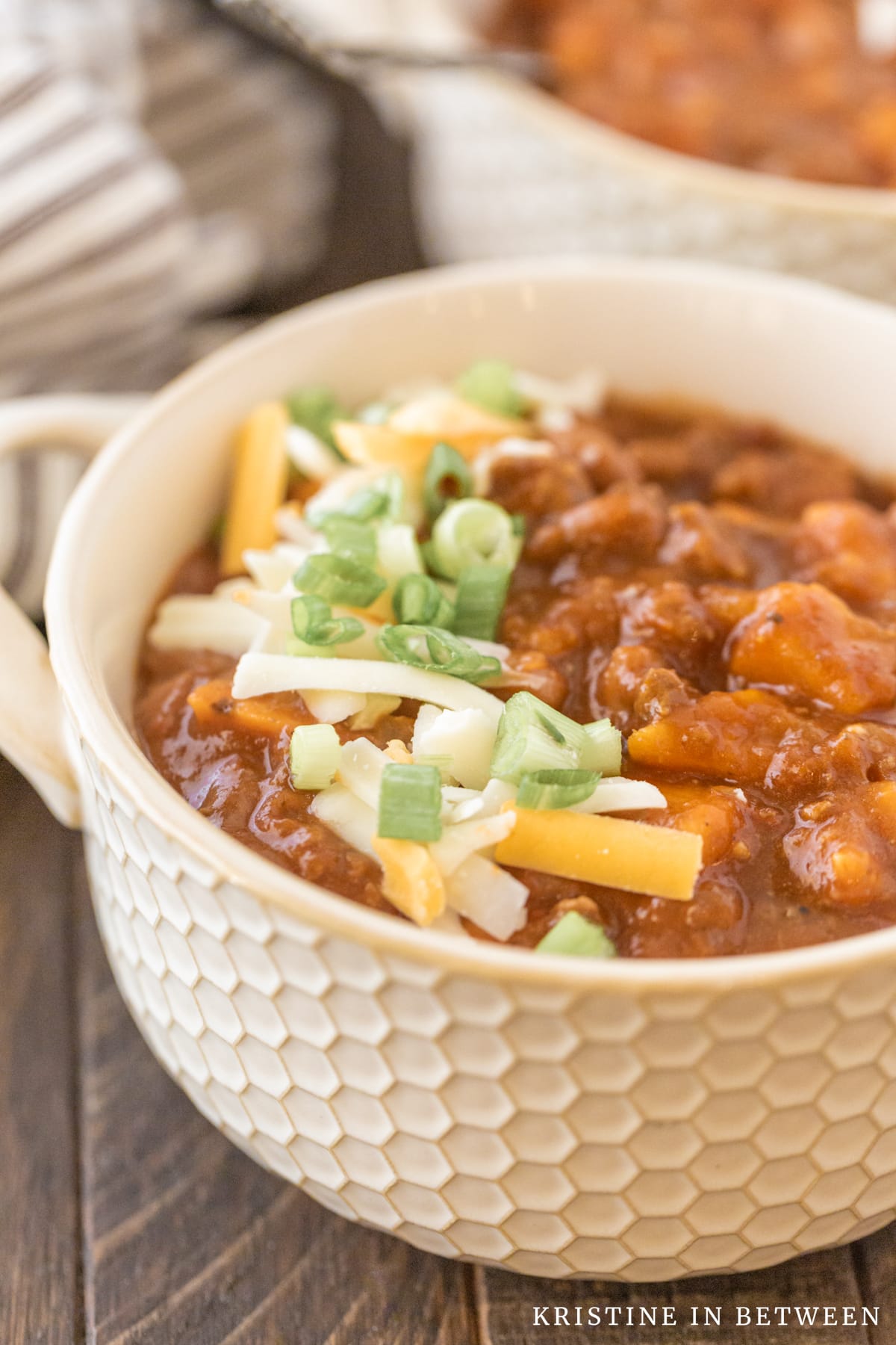A bowl of chili topped with cheese and green onion with a napkin in the background.