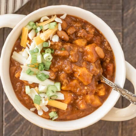 A bowl of sweet potato chili garnished with cheese and green onion with a spoon in it.