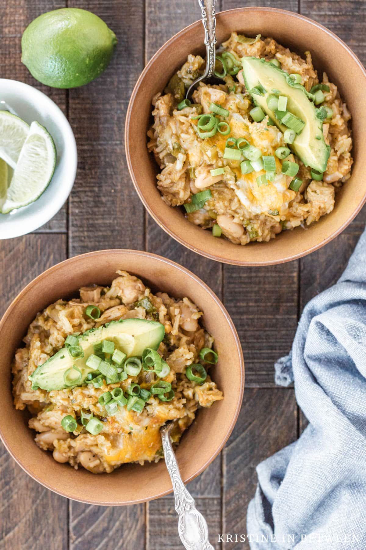 Two bowls of white chili with spoons in them, topped with avocado and green onions.