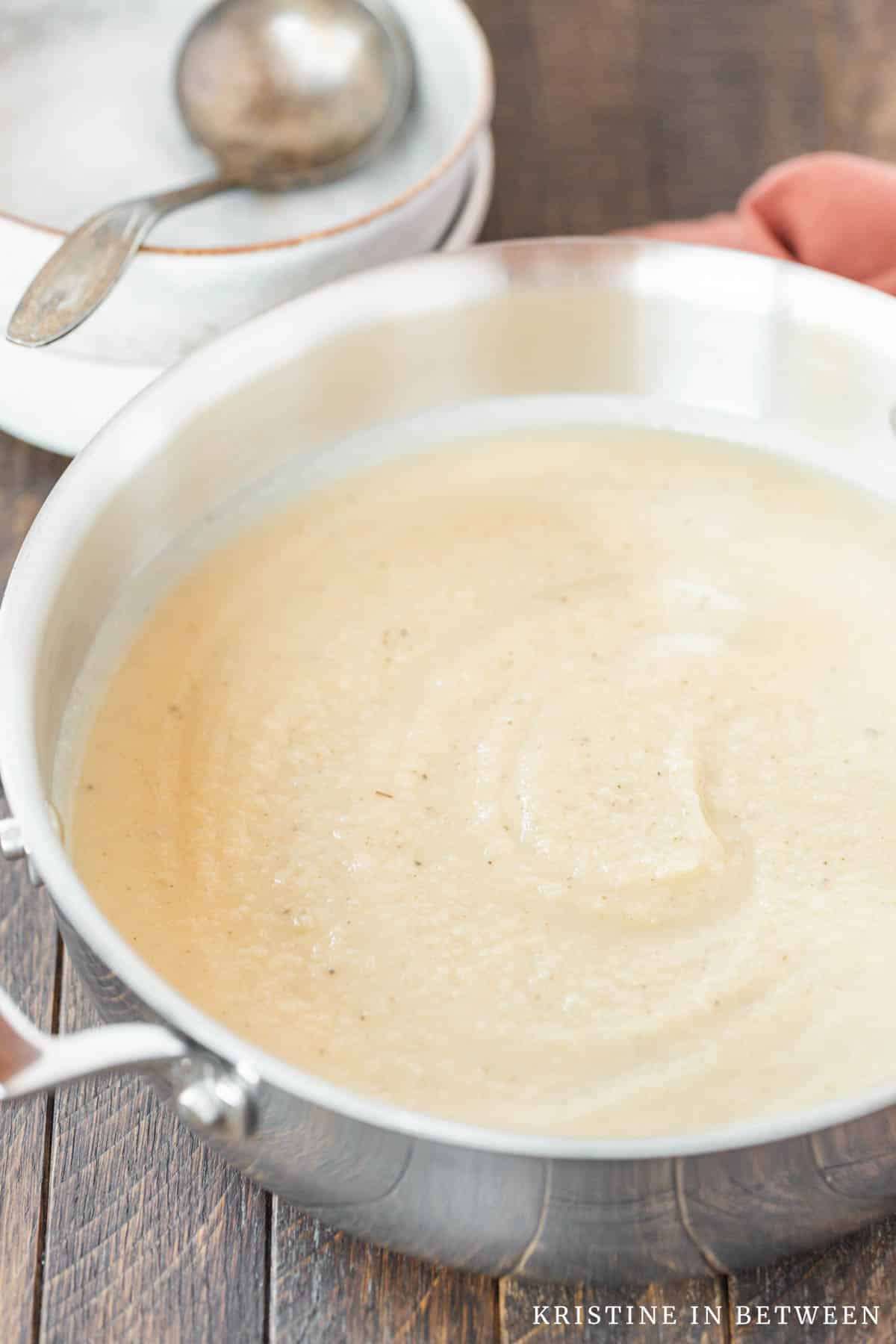 Cauliflower soup in the pan with two bowls and a ladle in the background.