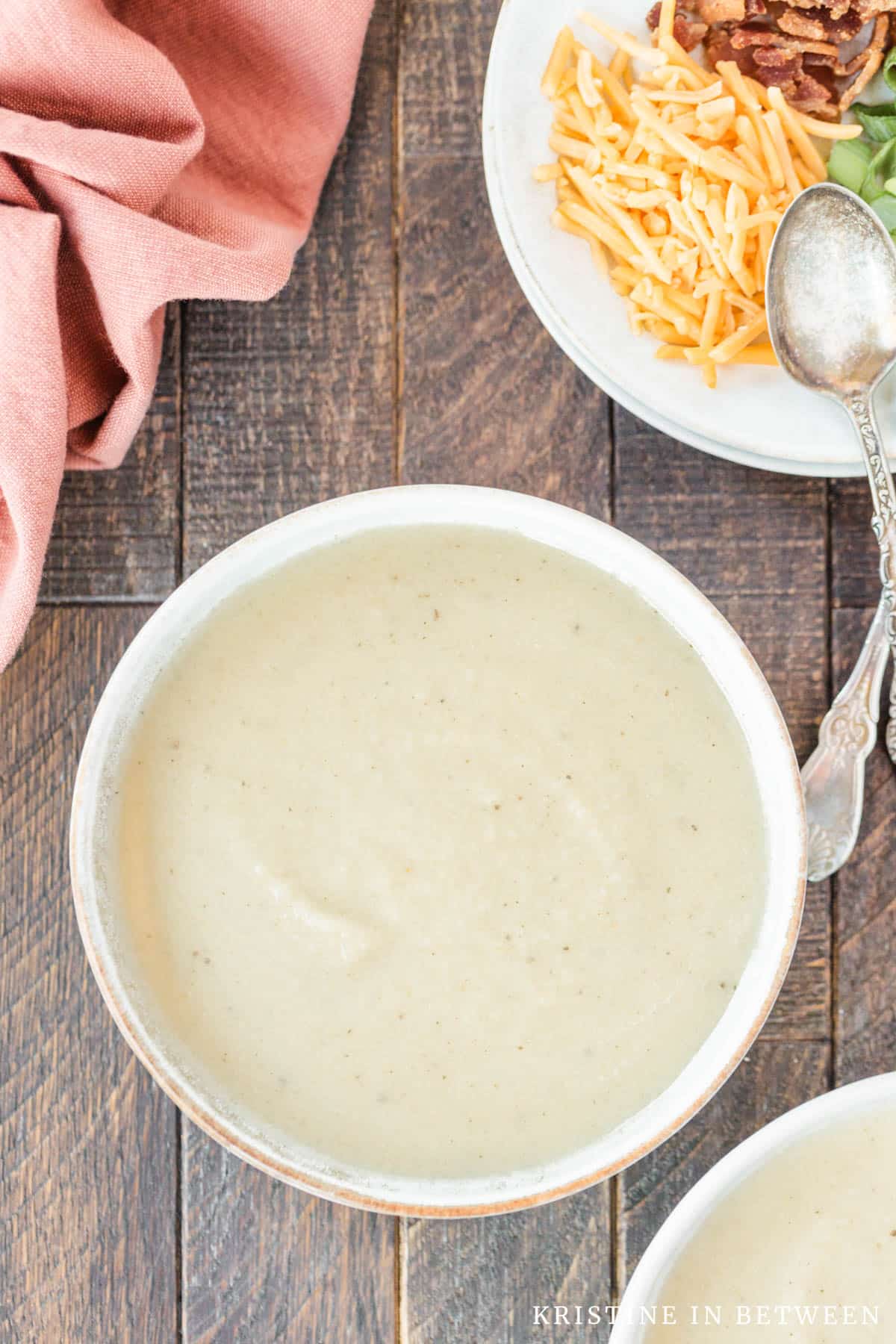 Plain cauliflower soup in a bowl with spoons laying next to it.