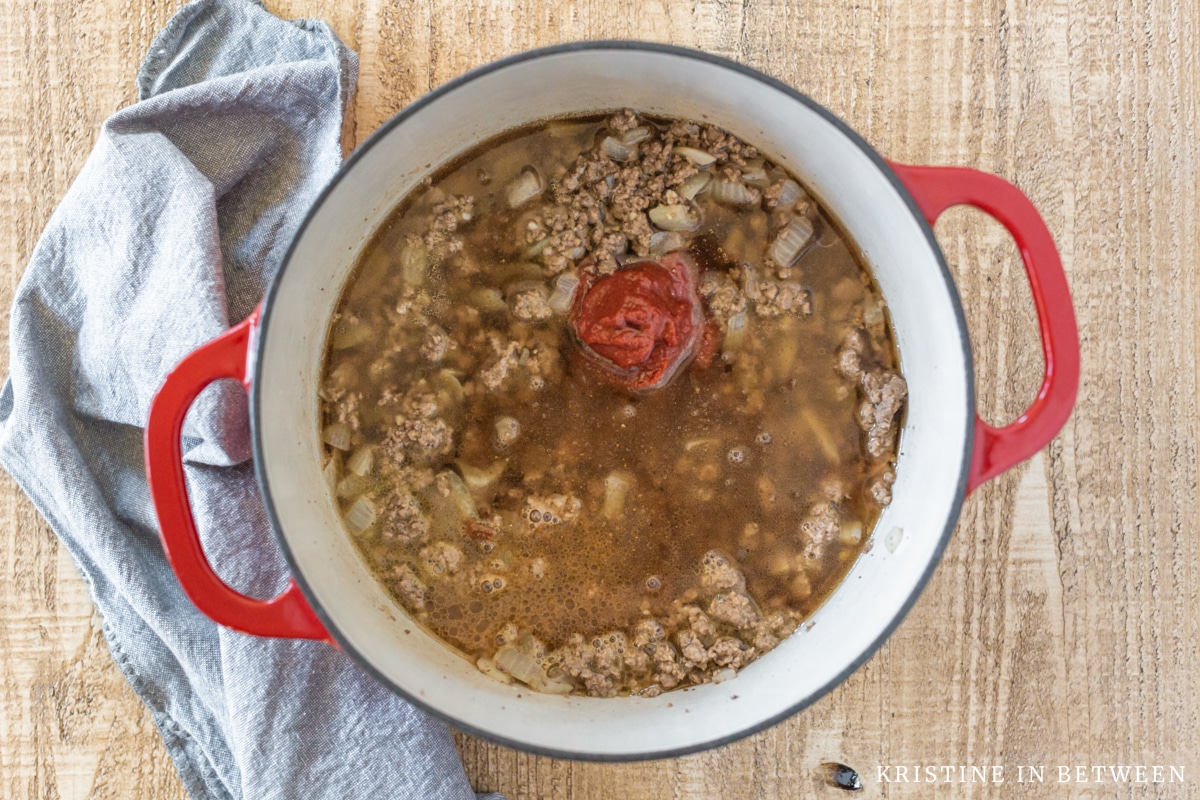 Cooked beef and onions with beef broth in a red Dutch oven.