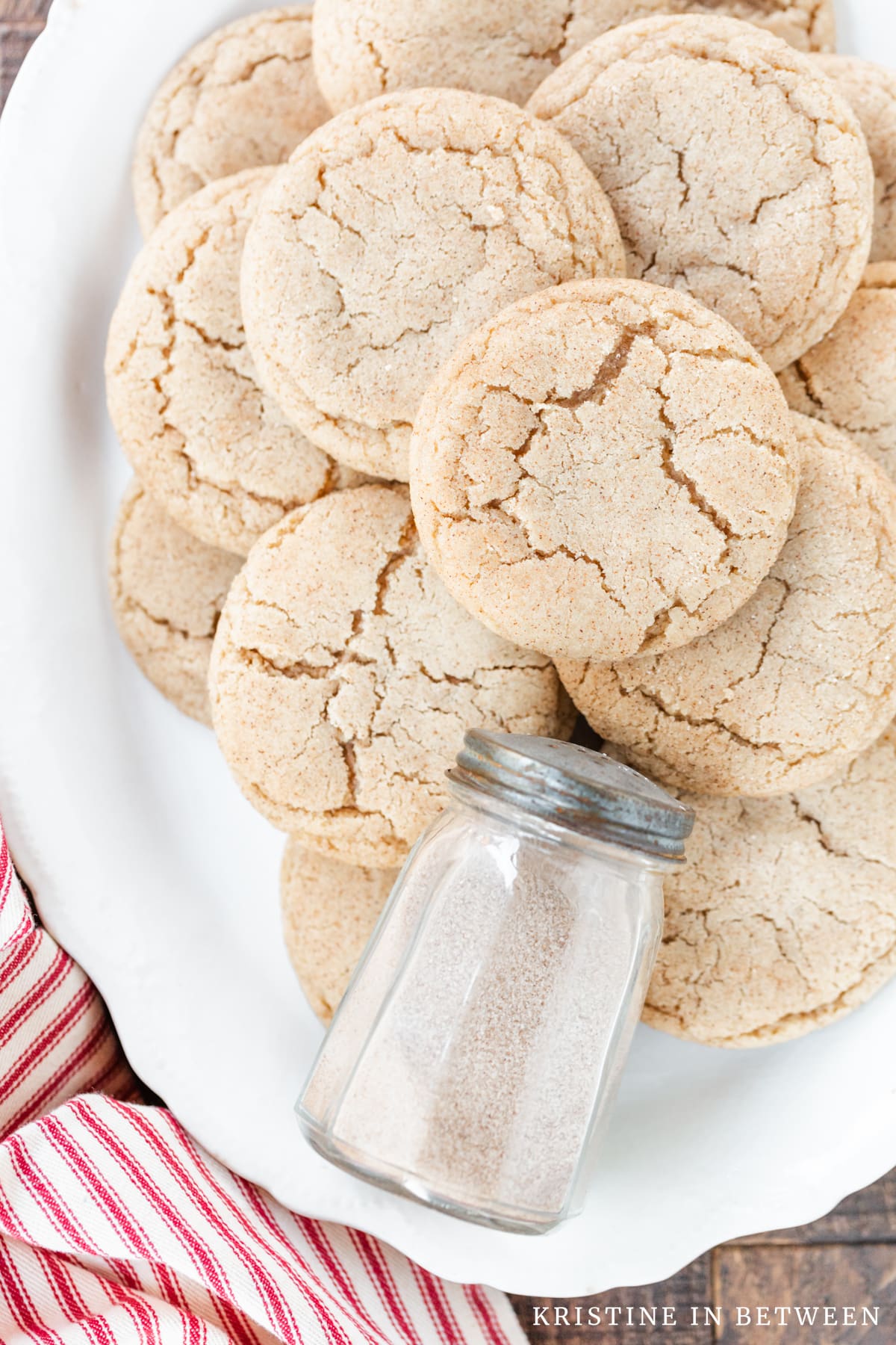 Cookies stacked up on a white platter with a shaker full of sugar sitting with them.