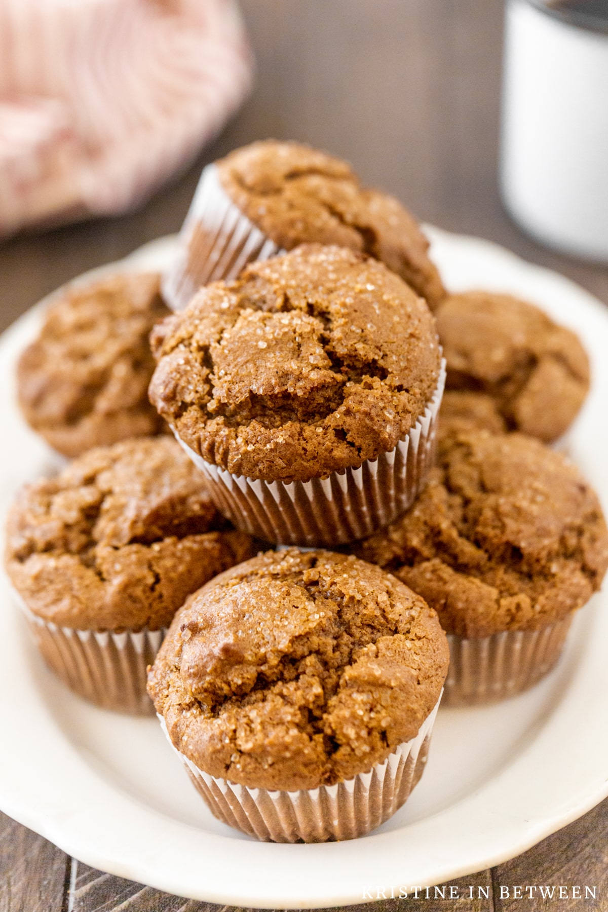 Muffins stacked up on a white plate with a cup of coffee in the background.