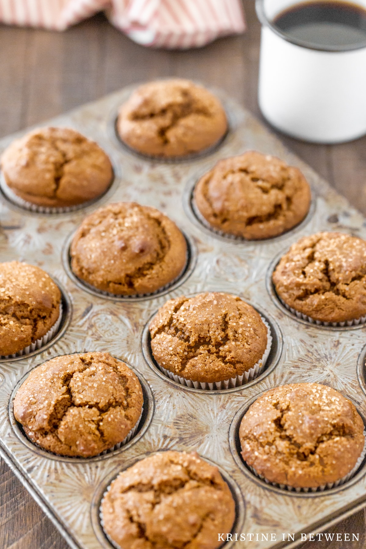 A muffin pan full of gingerbread muffins with a cup of coffee in the background.