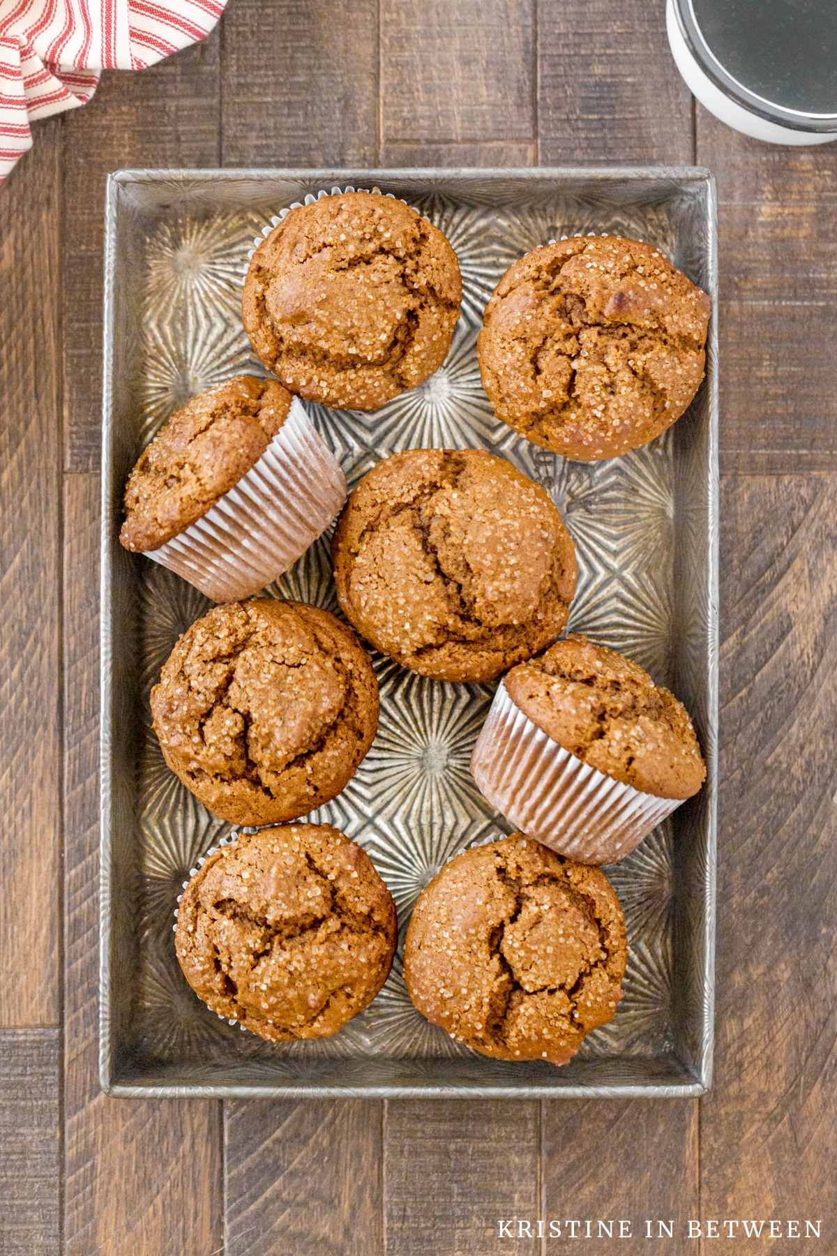 Muffins laying in a metal tin with a cup of coffee and a red striped napkin.