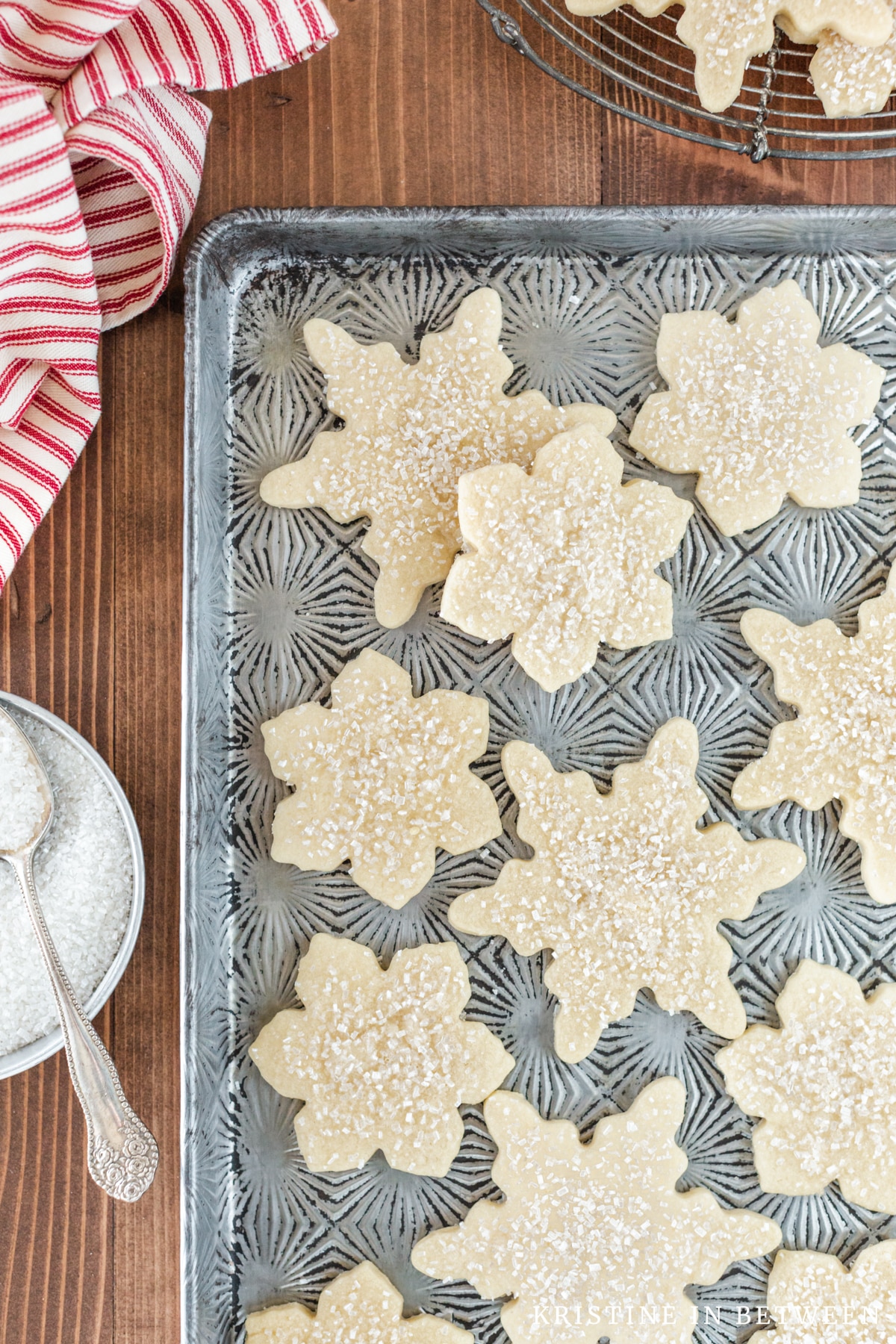 Cut out sugar cookies sitting on an antique baking sheet with a bowl of sugar next to them.