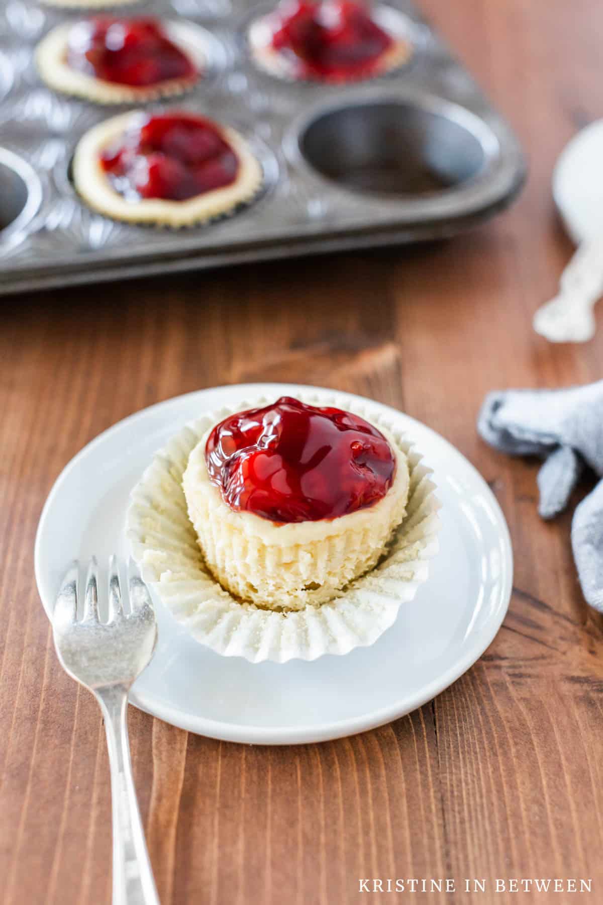 A tart sitting on a white plate with the wrapper pulled down and a fork next to it.