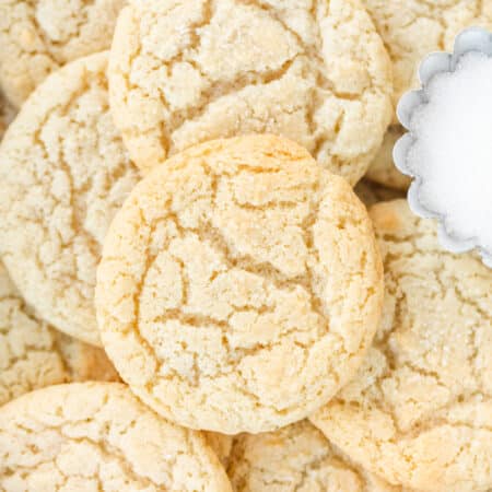 Sugar cookies stacked up with a small bowl of sugar.