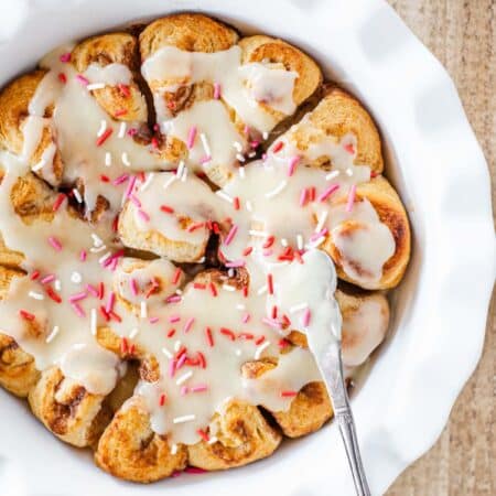 Frosted cinnamon rolls in a white pie plate with a small knife.