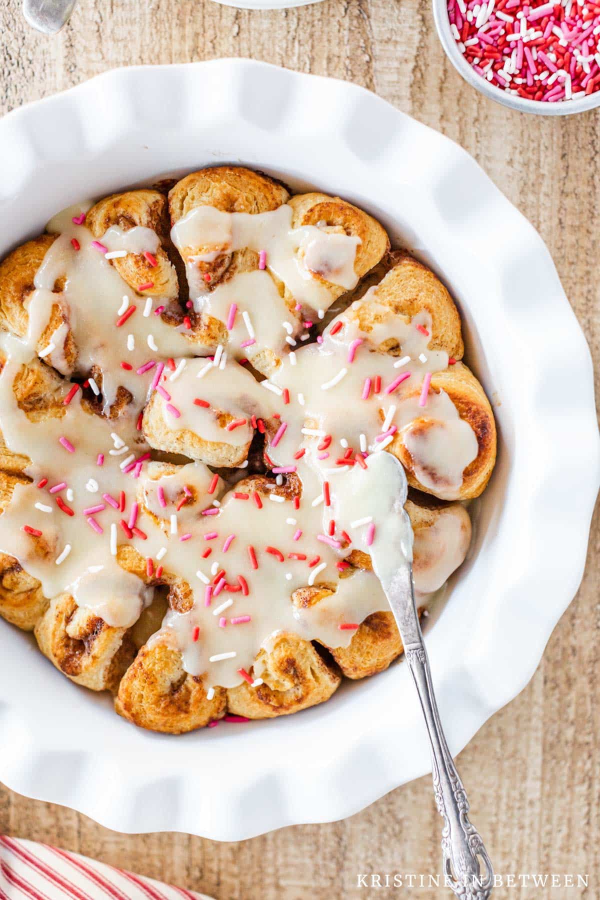 Frosted cinnamon rolls in a pie plate with a knife sitting next to them.