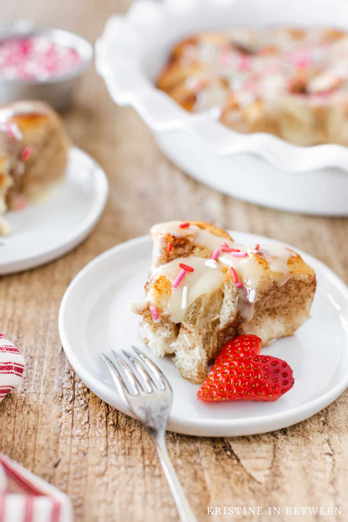 A cinnamon roll sitting on a plate with a strawberry and a fork.