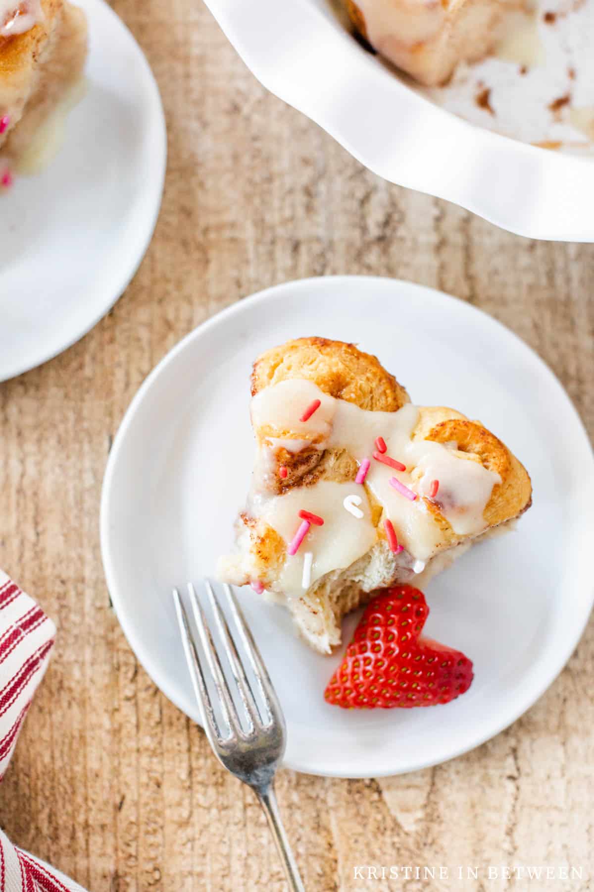 A cinnamon roll sitting on a white plate plate with a strawberry.