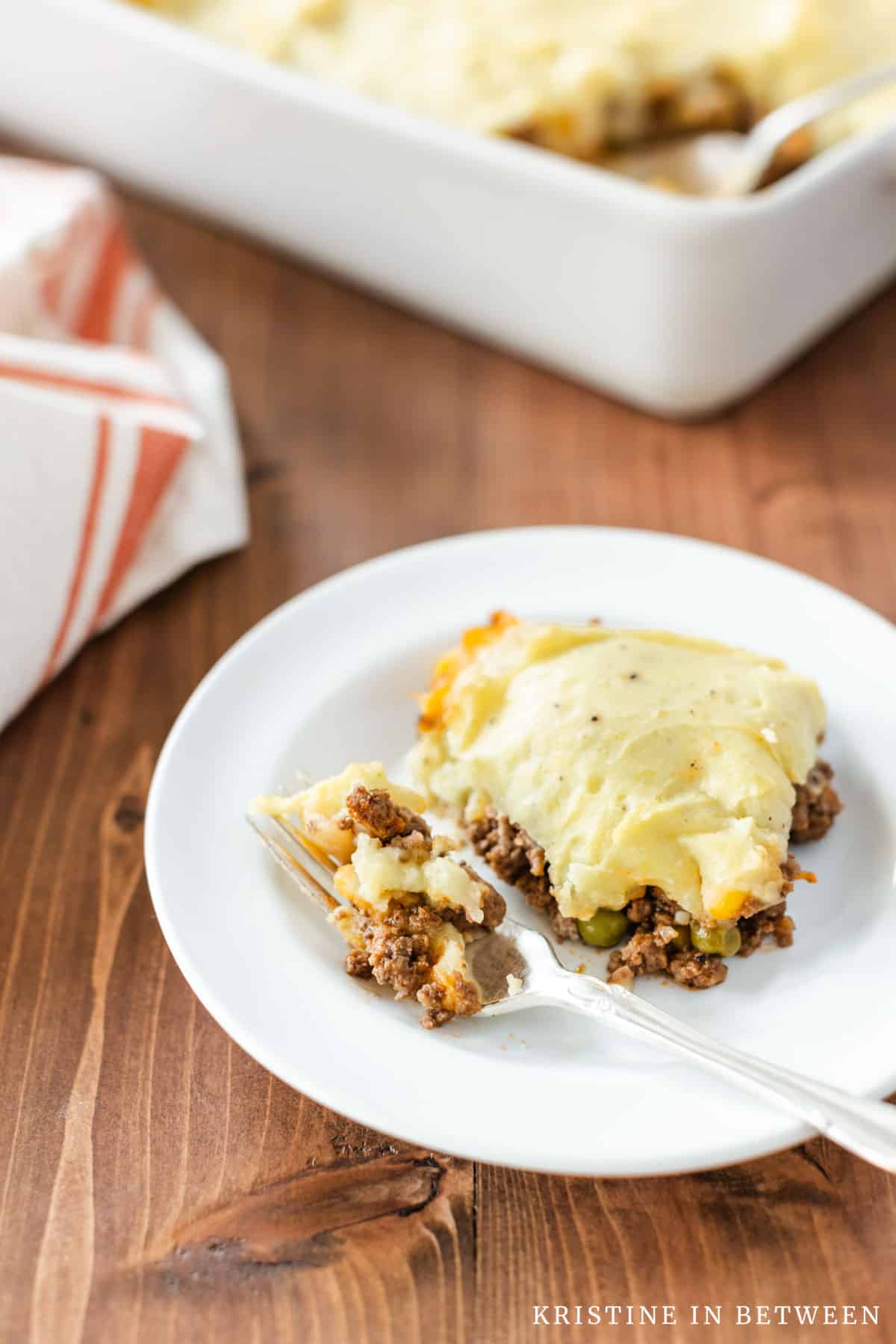 A plate of shepherd's pie with a fork sitting next to it and the rest of the pan in the background.