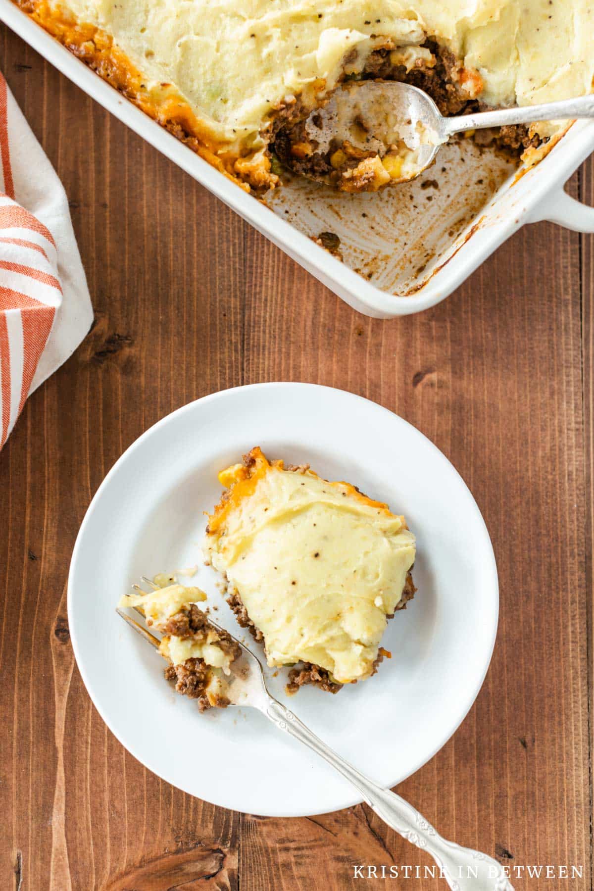 A plate of shepherd's pie with a bit on a fork and the rest of the pan in the background.