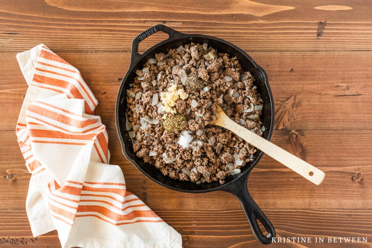 Cooked ground beef and onion in a cast iron skillet with spices sprinkled on top.