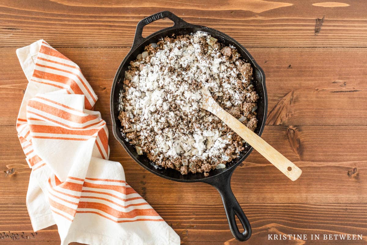 Cooked beef and onion in a cast iron skillet with flour sprinkled on top.