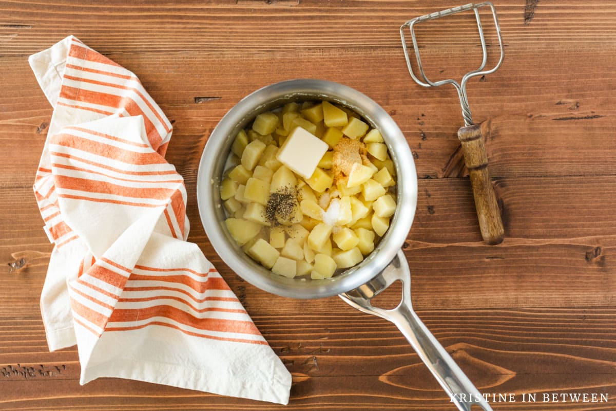 Cooked potatoes with butter, milk, salt, and pepper in a pan.