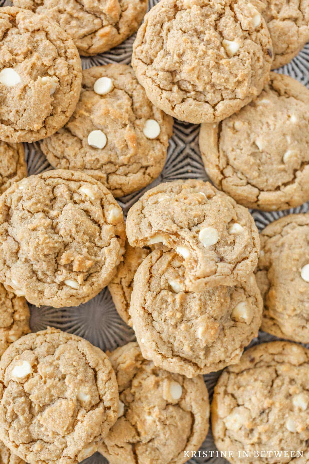 Cookies piled upon a baking sheet with the top one missing a bite.