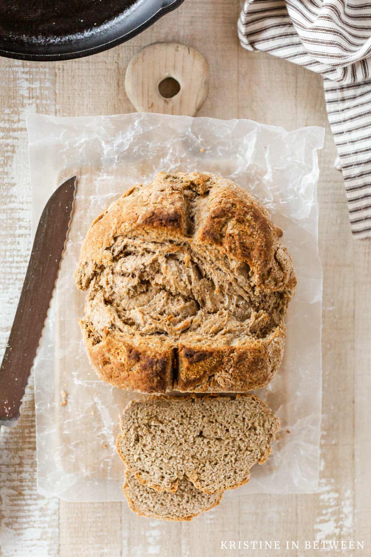 A loaf of brown bread with a few slices laying down and a bread knife next to it.