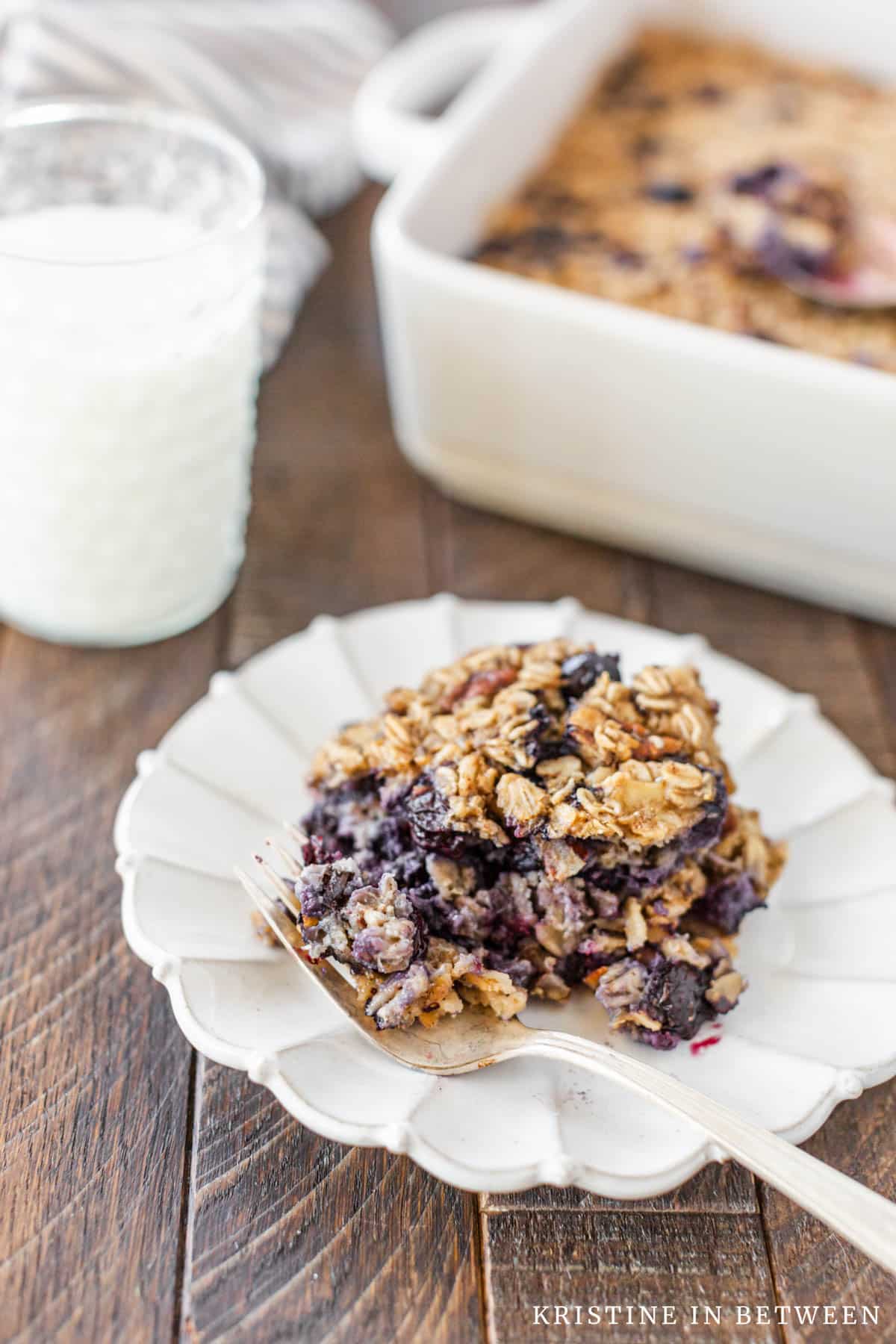 A small white plate with baked blueberry oatmeal on it and a fork with a bite on it.